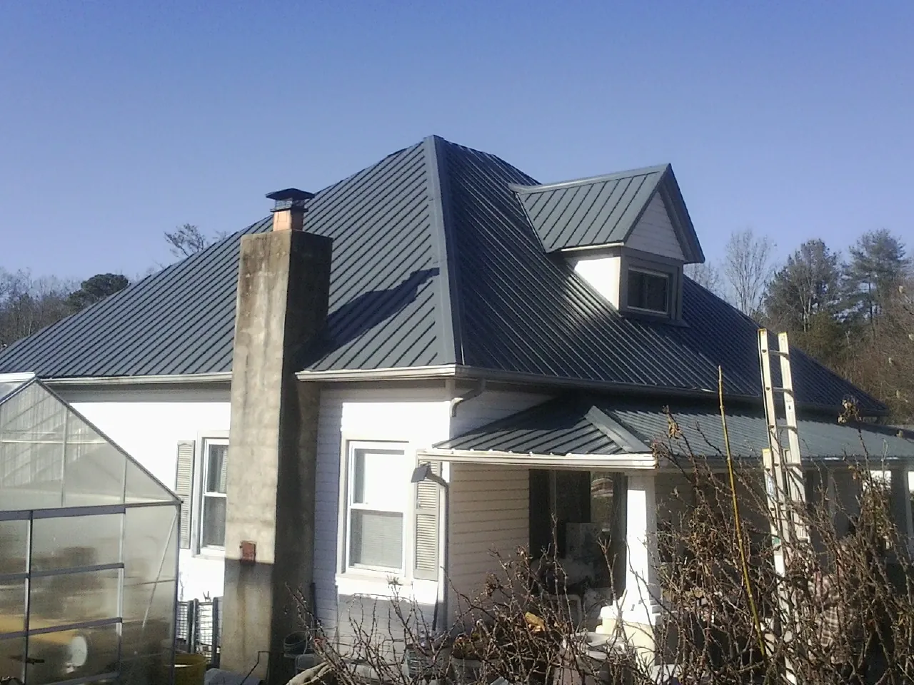Dark blue standing seam metal roof on a white farmhouse with dormer — Slate & Tile Roof Repair by Roofing Brothers in Kenilworth