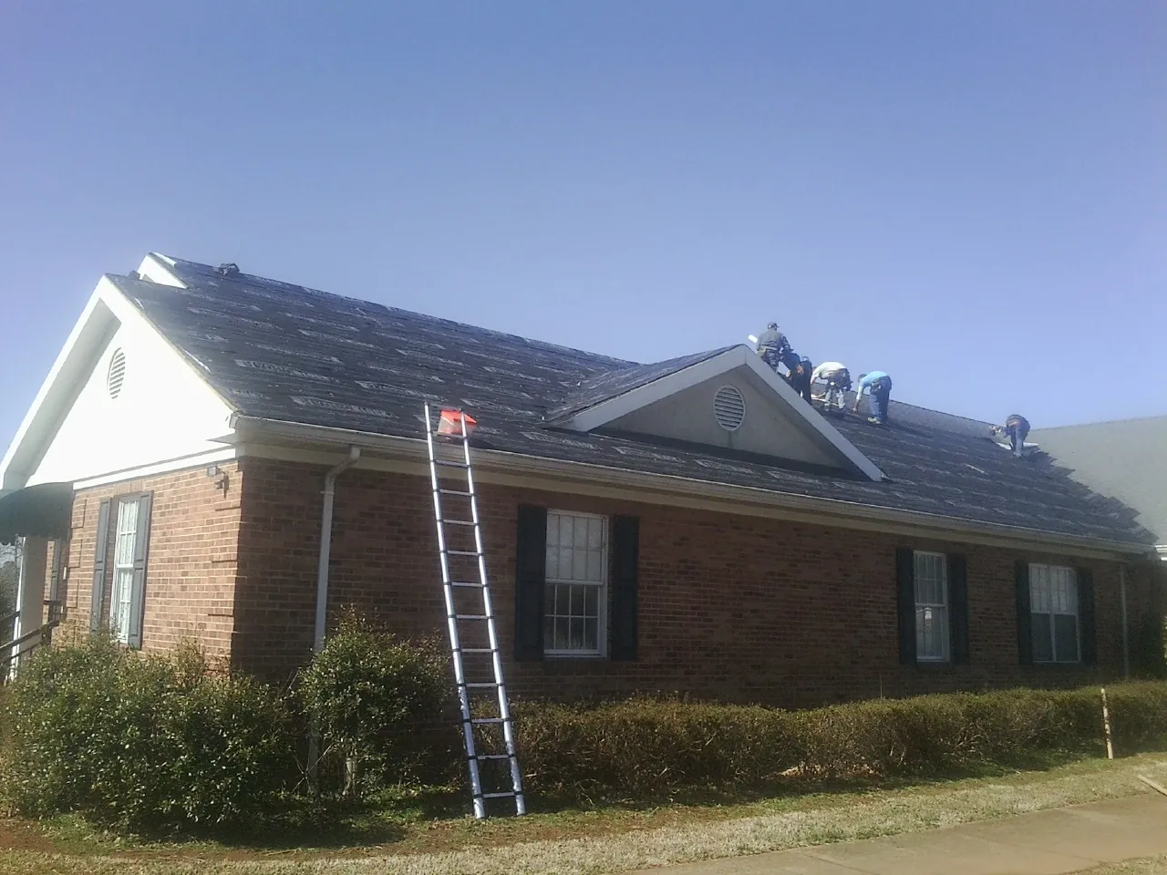 Crew tearing shingles off a brick ranch roof with a ladder set — Emergency Roof Repair work by our crew in Kenilworth