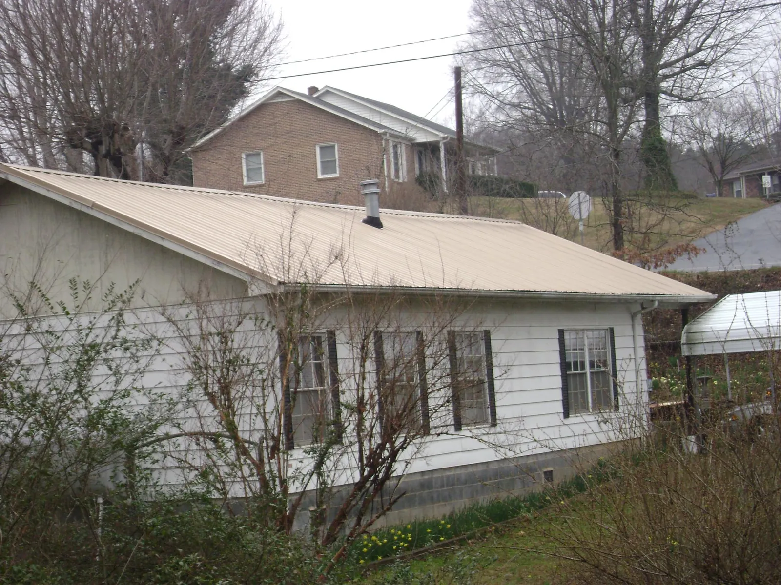 Tan metal roof on a white sided house set into a hillside — Commercial Roofing by Roofing Brothers in Kenilworth